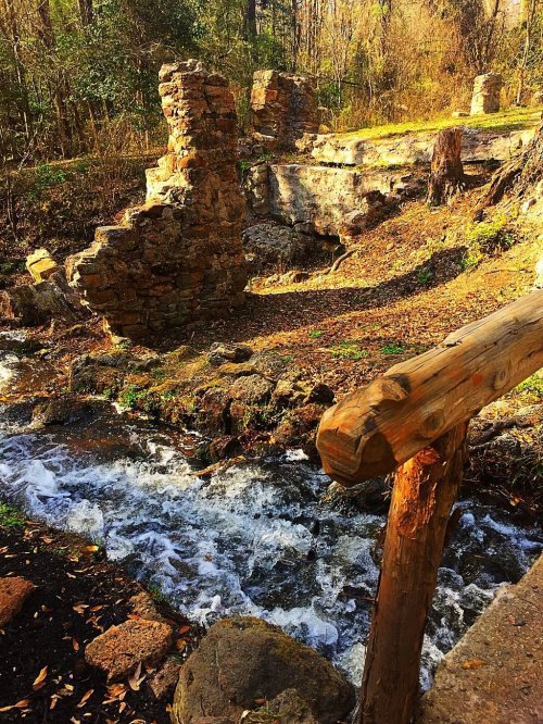 Ruins of a stone structure beside a flowing stream, surrounded by trees and autumn foliage.