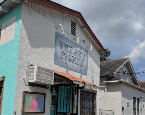 Exterior of Sneaky Pickles restaurant, featuring a colorful sign and a white building under a partly cloudy sky.