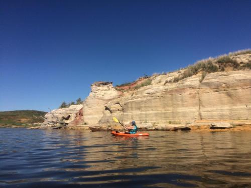 A person kayaking near colorful rock formations under a clear blue sky.
