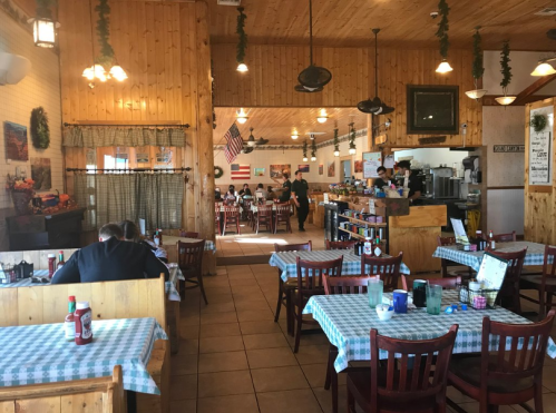 Cozy restaurant interior with wooden decor, checkered tablecloths, and patrons dining at tables. American flag visible.