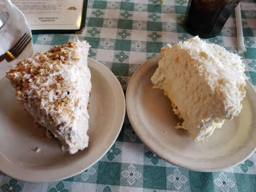 Two large slices of cake on plates: one topped with coconut and the other with a creamy frosting and nuts.