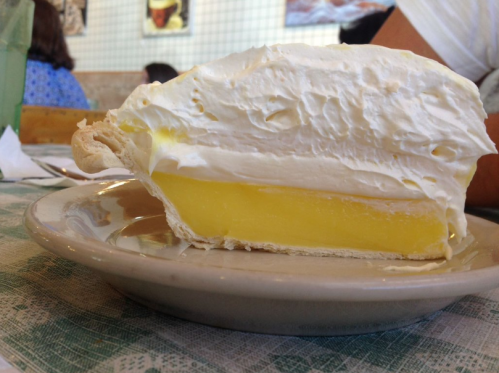 A slice of lemon meringue pie on a plate, featuring a smooth yellow filling and a fluffy white meringue topping.