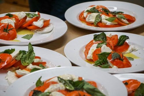 Plates of Caprese salad with sliced tomatoes, mozzarella, fresh basil, and drizzled olive oil.