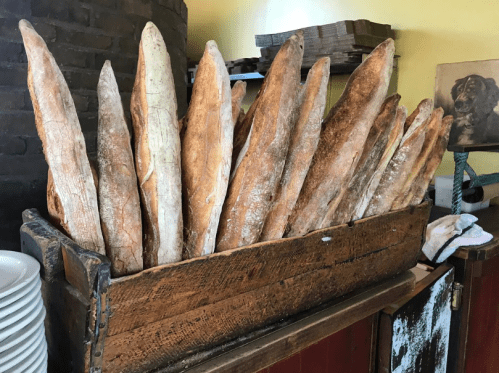 A wooden basket filled with freshly baked baguettes, displayed in a cozy bakery setting.