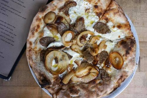 A pizza topped with sausage, caramelized onions, and a creamy white sauce on a charred crust.