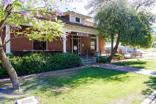 A charming brick building with a sign reading "Bar Banco," surrounded by greenery and purple flowers.