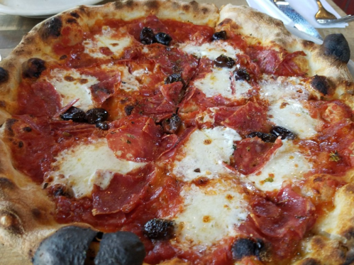 A close-up of a pizza topped with pepperoni, mozzarella, and black olives, with a crispy, charred crust.