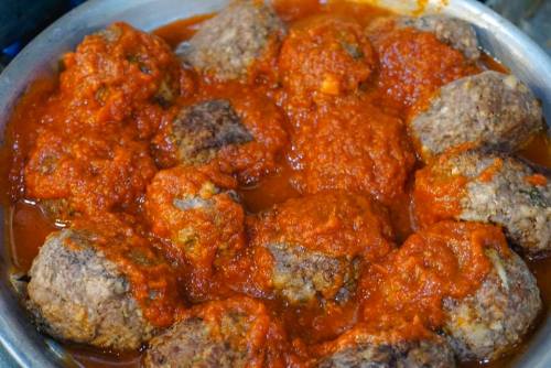 A close-up of meatballs simmering in a rich red tomato sauce in a metal dish.