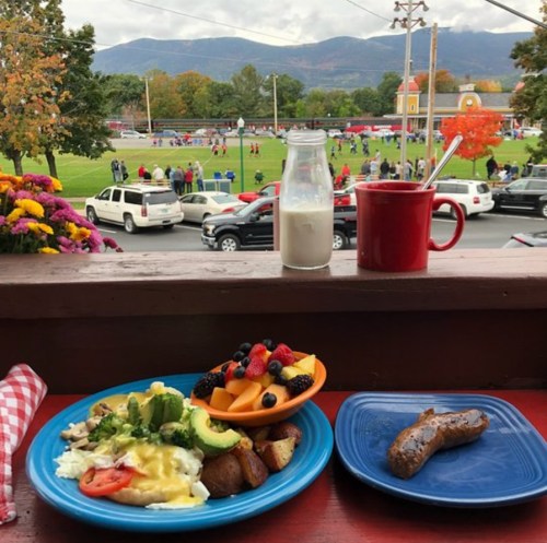 A scenic view of a park with a football game, featuring a breakfast plate with fruit, sausage, and a drink on a table.