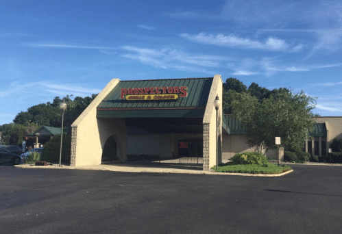 Exterior of Prospector's Grill & Saloon, featuring a green roof and a sign, surrounded by trees and a clear blue sky.