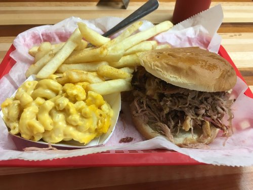 A red tray with a pulled pork sandwich, fries, and a side of macaroni and cheese.