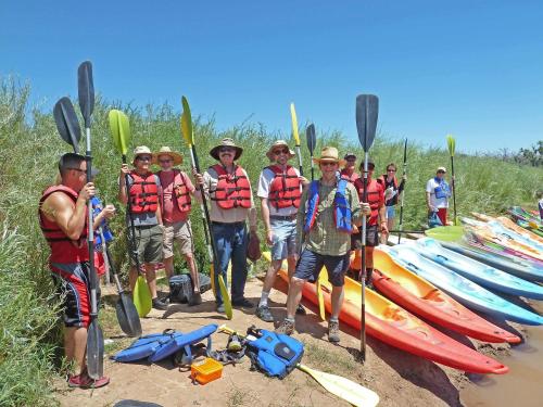 A group of people in life jackets holding paddles, standing by colorful kayaks on a sunny day.