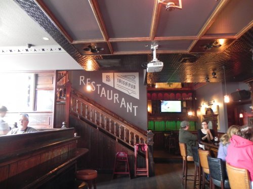 Interior of an Irish pub featuring a staircase, bar seating, and a sign that reads "Restaurant." Warm, inviting atmosphere.