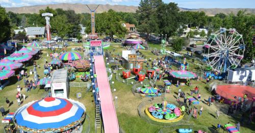 Aerial view of a vibrant carnival with rides, games, and colorful tents, bustling with visitors enjoying the festivities.