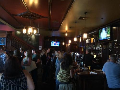 A lively bar scene with patrons chatting, a bartender serving drinks, and TVs showing sports in a warm, inviting atmosphere.