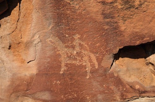 Petroglyph of a rider on a horse carved into a reddish rock surface, showcasing ancient artistic expression.