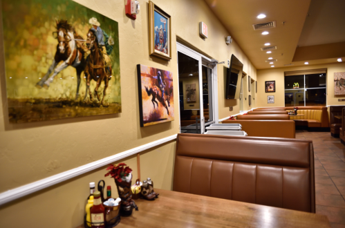 Interior of a restaurant featuring horse-themed artwork, booths, and condiments on a table. Warm, inviting atmosphere.