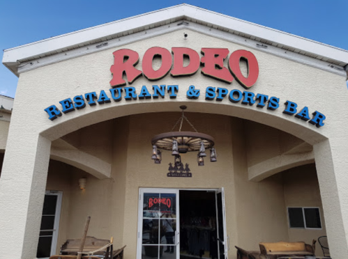 Exterior of Rodeo Restaurant & Sports Bar, featuring a large sign and a decorative chandelier. Clear blue sky above.