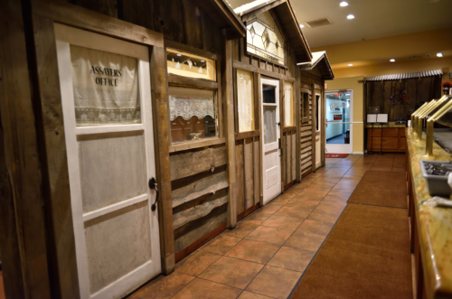 A rustic hallway with wooden doors resembling small cabins, leading to various offices in a cozy setting.