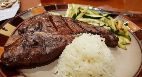 A plate featuring a grilled steak, seasoned rice, and sautéed zucchini and carrots.