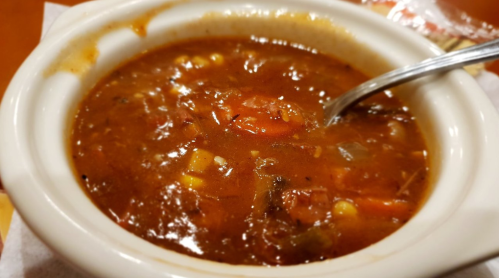 A bowl of hearty vegetable soup with tomatoes, corn, and spices, served with a spoon.