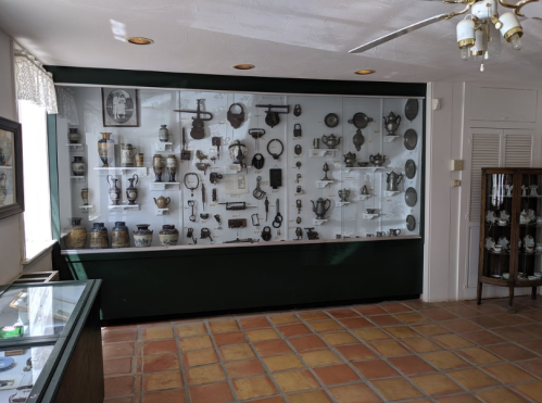 Display case filled with various antique items, including tools and utensils, in a well-lit room.
