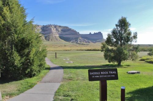 A scenic view of Saddle Rock Trail, leading through grassy terrain with a rocky formation in the background.