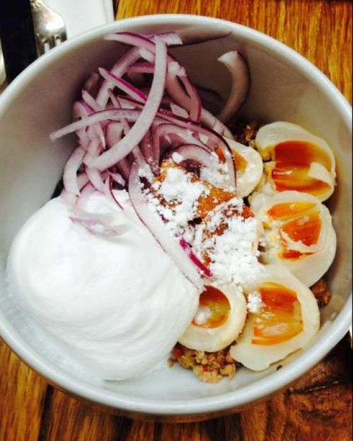 A bowl of food featuring sliced onions, creamy topping, and halved eggs on a bed of grain or meat.