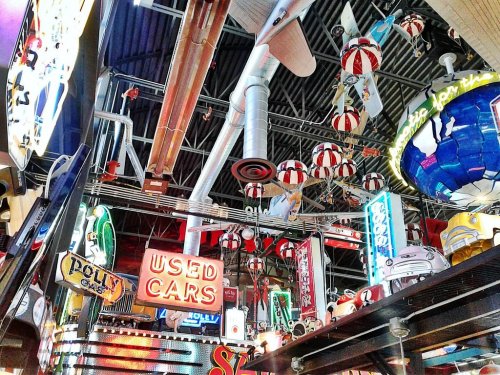 Colorful vintage signs and decorations hang from the ceiling, creating a vibrant, eclectic atmosphere indoors.
