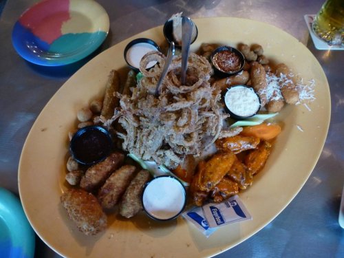 A large platter of assorted fried foods, including wings, onion rings, and dipping sauces, served on a colorful plate.