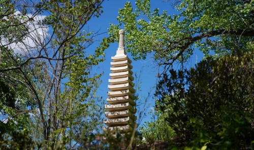 A tall, white pagoda surrounded by green trees and blue sky, showcasing a serene outdoor setting.