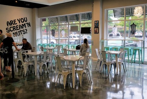 A bright café interior with metal tables and chairs, featuring a playful sign and large windows showing the street outside.