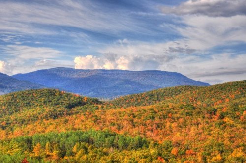 Vibrant autumn landscape with rolling hills, colorful foliage, and a distant mountain under a cloudy sky.