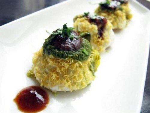 Three savory Indian snacks topped with green chutney, tamarind sauce, and garnished with herbs on a white plate.