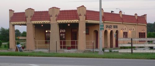 Historic building with a red-tiled roof, arched windows, and a sign reading "Shady Bend," set along a roadside.