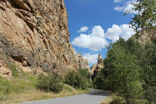 A scenic road winds through towering rock formations and lush greenery under a blue sky with fluffy clouds.