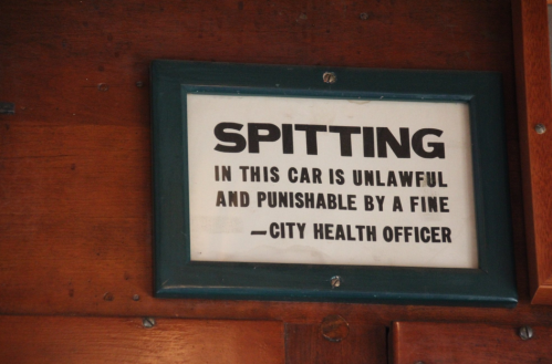 Sign on a wooden wall stating "Spitting in this car is unlawful and punishable by a fine - City Health Officer."