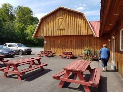 A wooden building with a red roof, surrounded by picnic tables, and a person walking towards the entrance.