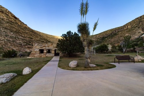 A scenic view of a park with stone structures, trees, and mountains under a clear blue sky.