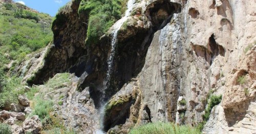 A scenic waterfall cascading down rocky cliffs, surrounded by lush greenery and natural rock formations.