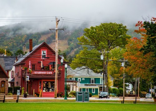 A red café building with a sign, surrounded by trees and mountains, under a cloudy sky. Power lines in the foreground.