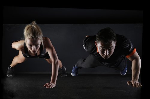Two individuals performing push-ups on a dark surface, focused and in athletic attire.