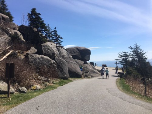 A scenic pathway leads through rocky terrain with people enjoying the outdoors under a clear blue sky.