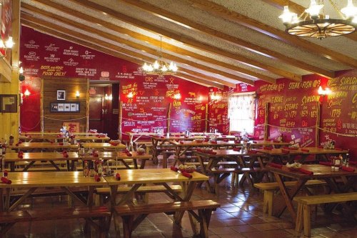 A rustic restaurant interior with wooden tables, benches, and vibrant red walls covered in menu items and decor.