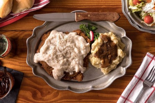 A plate of chicken fried steak topped with gravy, served with mashed potatoes and a side of salad.