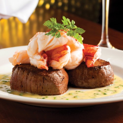 A gourmet dish featuring two filet mignon topped with shrimp and garnished with parsley, served on a white plate.
