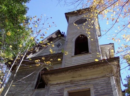 An old, weathered building with a tower, surrounded by trees and autumn leaves under a clear blue sky.