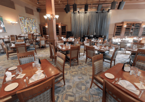 A spacious restaurant interior with wooden tables, chairs, and a stage, featuring elegant decor and wine storage.