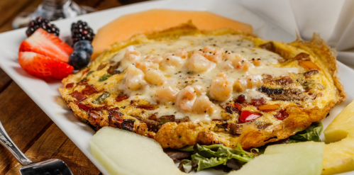 A delicious omelette topped with shrimp and cheese, served with fresh fruit and melons on a white plate.