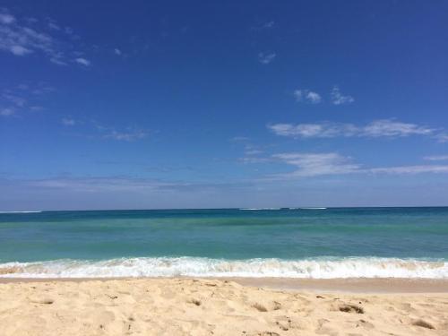 A serene beach scene with golden sand, clear blue water, and a bright sky with scattered clouds.
